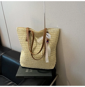 Detail of hand-woven straw tote with brown leather strap and decorative lace pendant