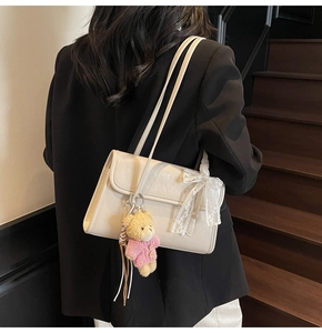 Détail d'un sac sous le bras blanc crème avec nœud en dentelle et pendentif ours