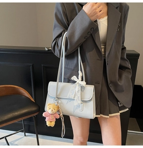 Détail du sac bandoulière en cuir verni bleu clair avec nœud dentelle et charm ours
