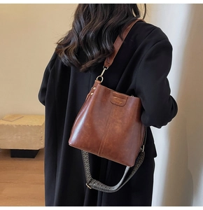 Detail of a brown leather bucket bag featuring a textured wide fabric strap and gold hardware