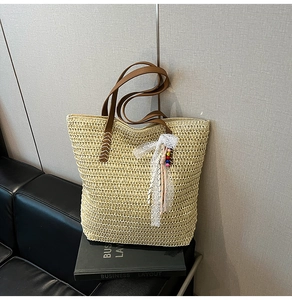 Detail of woven straw tote bag featuring brown leather straps and lace bead charms