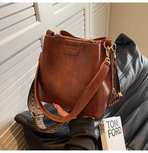 Detail of brown bucket bag featuring embossed logo and ethnic geometric wide strap