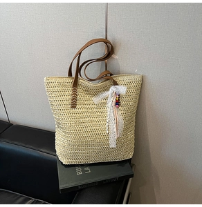 Detail of woven straw tote bag with brown leather handles and lace bead pendant charm