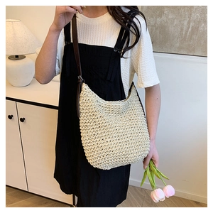 Detail of a beige woven straw bucket bag with an adjustable dark brown leather strap