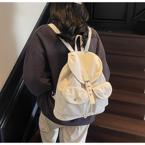 Detail view of a cream-white backpack featuring a drawstring closure and dual front pockets