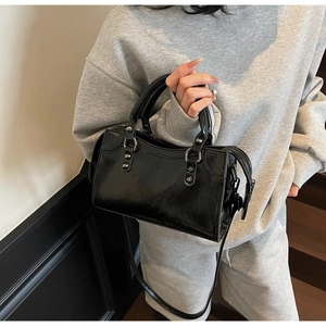 Détail d'un sac à main noir brillant avec rivets en métal et bandoulière réglable