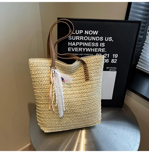 Detail of light beige straw tote bag featuring brown leather handles and lace tassel