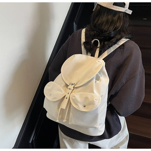 Side view of cream-white canvas backpack showing side profile and flap buckle on model