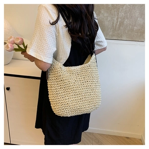 Detailed close-up of a beige woven straw bucket bag with dark leather shoulder strap details