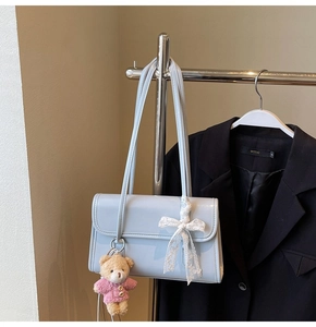 Détail du sac bandoulière en cuir verni bleu clair avec nœud en dentelle et ours