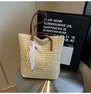 Detail of hand-woven straw tote bag showing brown leather handles and lace charm