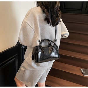 Sac Boston noir chic en similicuir brillant porté avec une tenue de loisirs grise