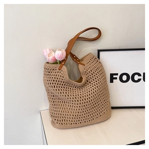 Detail of hand-woven straw tote with brown leather strap and sturdy metal rivets