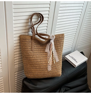 Detail of straw woven tote bag featuring white lace and pink tassel charms