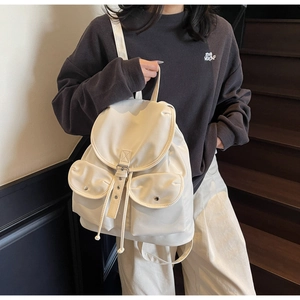 Detailed close-up of cream nylon backpack featuring symmetrical flap pockets and metal buckles