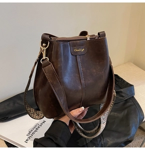 Detail of dark brown leather bucket bag featuring gold logo and textured woven strap