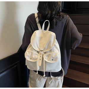 Close-up of a cream white nylon backpack with drawstring flap and metal buckles on steps
