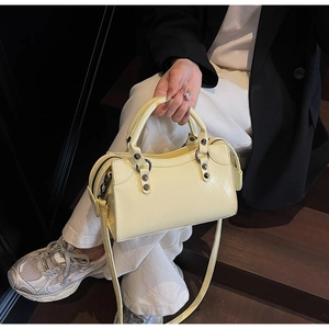 Détail du sac carré jaune pâle avec texture froissée et rivets vintage sur un escalier