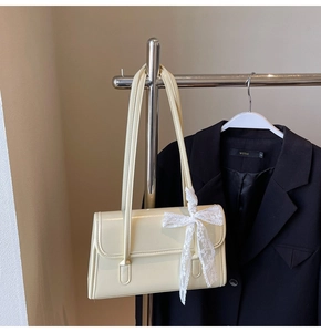 Détail du sac à bandoulière en similicuir crème avec un nœud décoratif en dentelle blanche