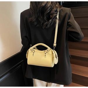 Détail d'un sac en cuir crème avec boucle métallique et poignée porté par un mannequin