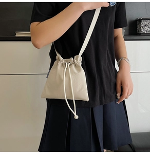 Detailed view of a beige drawstring nylon bucket bag worn by a model in a minimalist setting