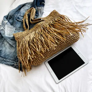 Close-up of a large woven straw tote bag featuring dense brown fringes in a lifestyle setting