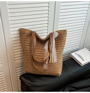 Detail of woven straw tote bag featuring leather handles and white lace decorative ribbon