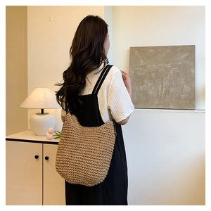 Detail of hand-woven straw shoulder bag showing large capacity and soft texture on a model