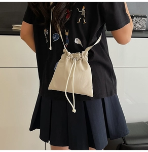 Detailed overhead view of a beige nylon drawstring bucket bag on a minimalist model outfit