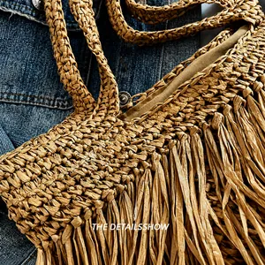 Close-up of handwoven straw tote bag with long fringe tassels and braided handle detail