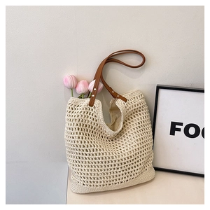 Detail of woven straw tote bag with brown faux leather handles and silver rivets