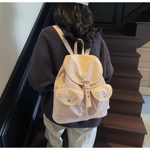 Detail view of a cream canvas backpack featuring a flap closure and double front pockets