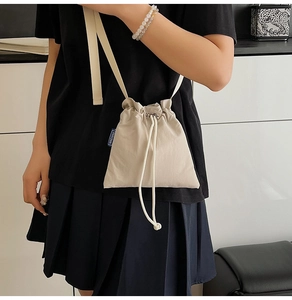 Detailed shot of beige nylon drawstring bucket bag with branded label and strap