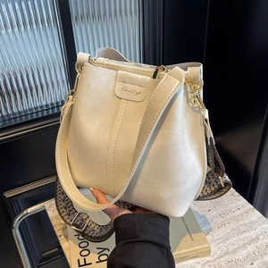 Close-up of cream leather bucket bag featuring a wide jacquard strap and gold zipper