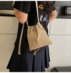 Detail view of the khaki drawstring bucket bag with adjustable strap and side blue label