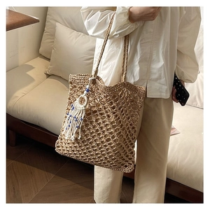Close-up of woven straw tote bag featuring intricate hollow mesh and white tassel charm