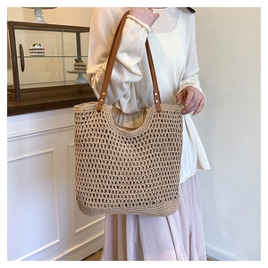 Detail of hollow woven straw tote bag with brown faux leather shoulder straps and rivets