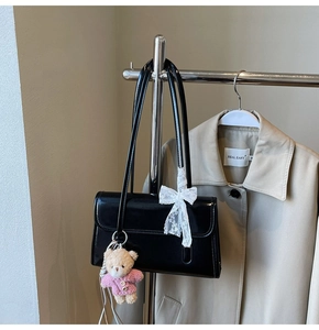Détail d'un sac d'épaule en cuir verni noir avec un nœud en dentelle blanche et un ours en peluche