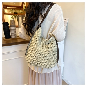Detail of hand-woven beige straw bucket bag with adjustable dark brown faux leather strap