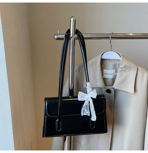 Détail du sac bandoulière en cuir verni noir avec nœud en dentelle blanche sur cintre