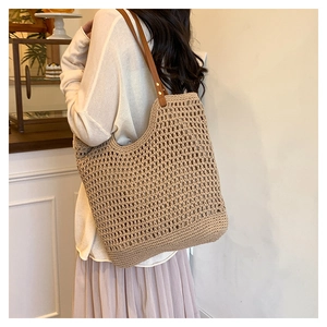 Detail view of woven straw tote bag featuring brown leather straps and gold rivets