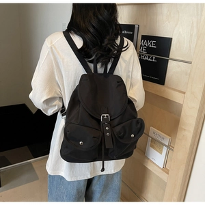 Fashionable black nylon backpack with metal buckles shown on a model in a minimal setting