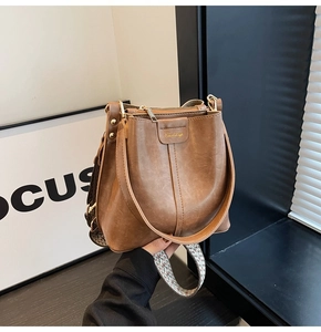 Brown leather bucket bag with colorful woven strap and golden zipper details