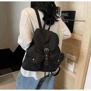 Rear view of model wearing a black nylon backpack with buckle closure and pockets