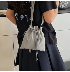Detail view of a light gray nylon drawstring crossbody bag with a blue brand label