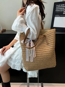 Large woven straw tote bag with brown leather straps and floral tassel detail on model