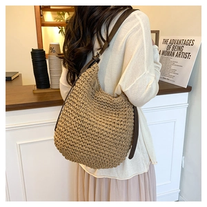 Detailed view of the woven straw bucket bag with dark brown leather strap worn by a model