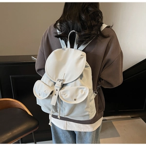 Detail showing light gray nylon backpack with dual front pockets and silver metal buckles