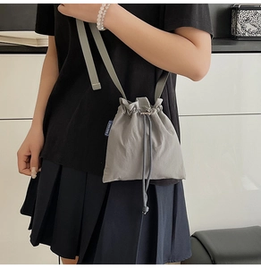Detail of grey nylon drawstring crossbody bucket bag showing lightweight pleated fabric