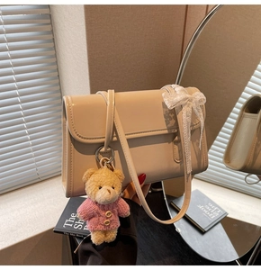 Détail du sac beige avec nœud en dentelle et charmant petit ours en peluche avec un pull